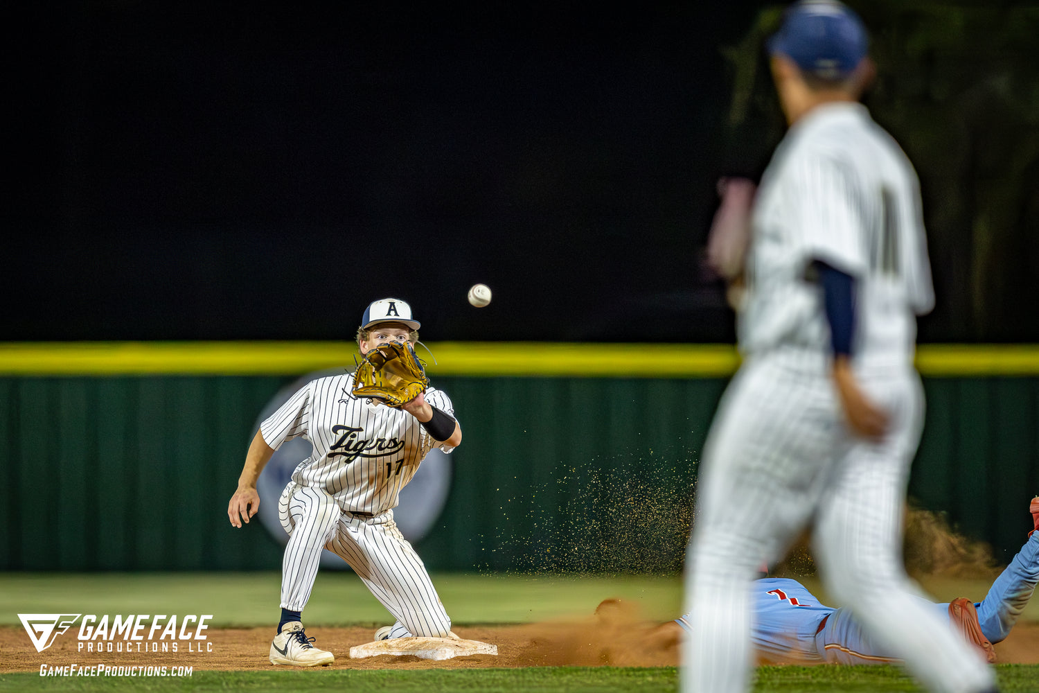 Baseball player in a striped uniform catching a ball on a field with another player in the background.